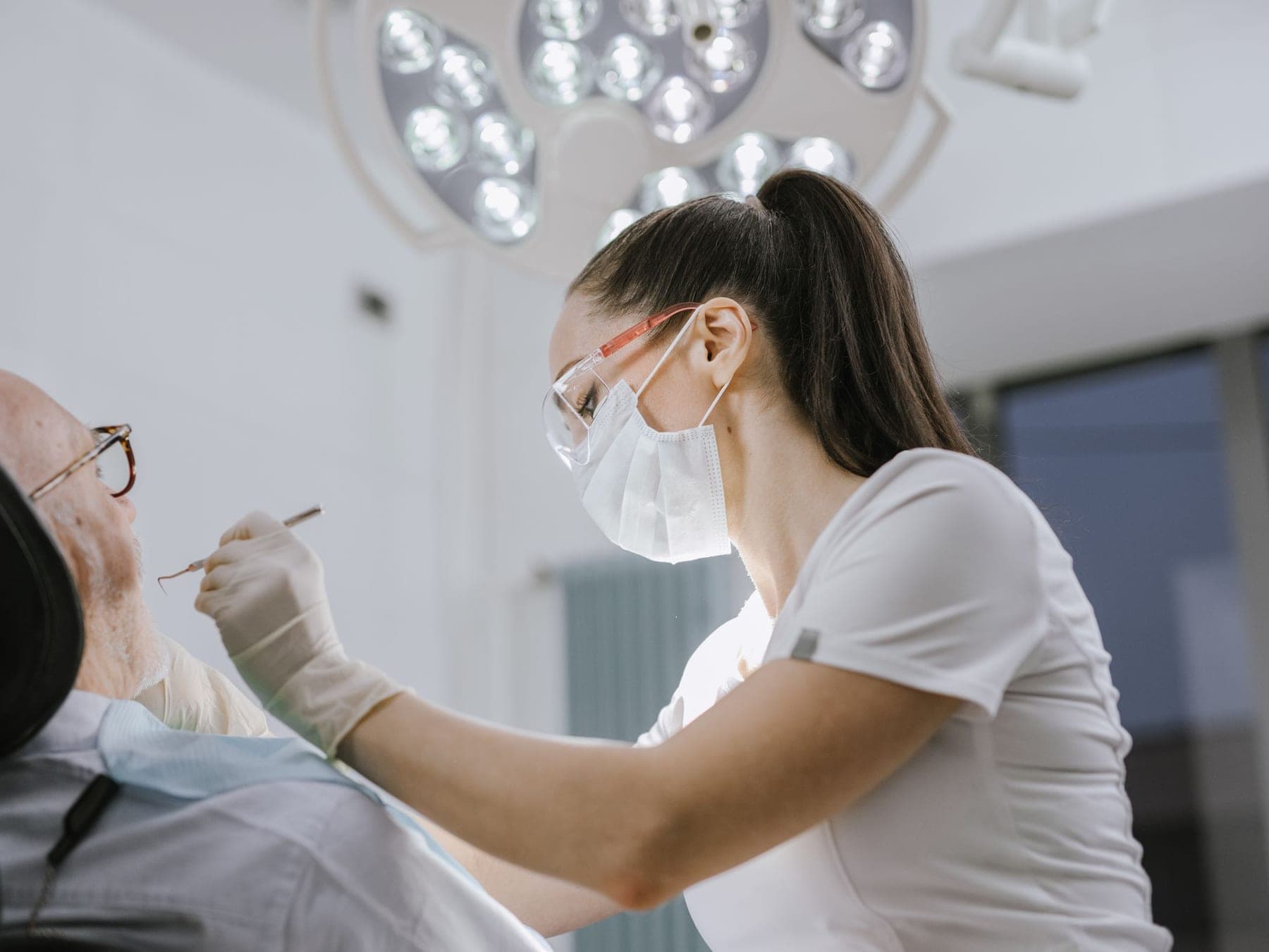 Zahnärztin mit Schutzbrille behandelt einen älteren Patienten